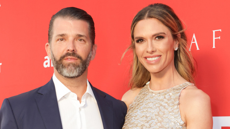 Bettina Anderson smiling in a gold dress next to Donald Trump Jr. who's wearing a blazer and white collared shirt.